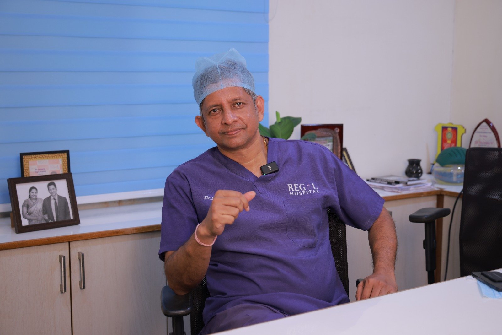 Dr. V. Suriraju seated in surgical scrubs at Regal Hospital Bengaluru